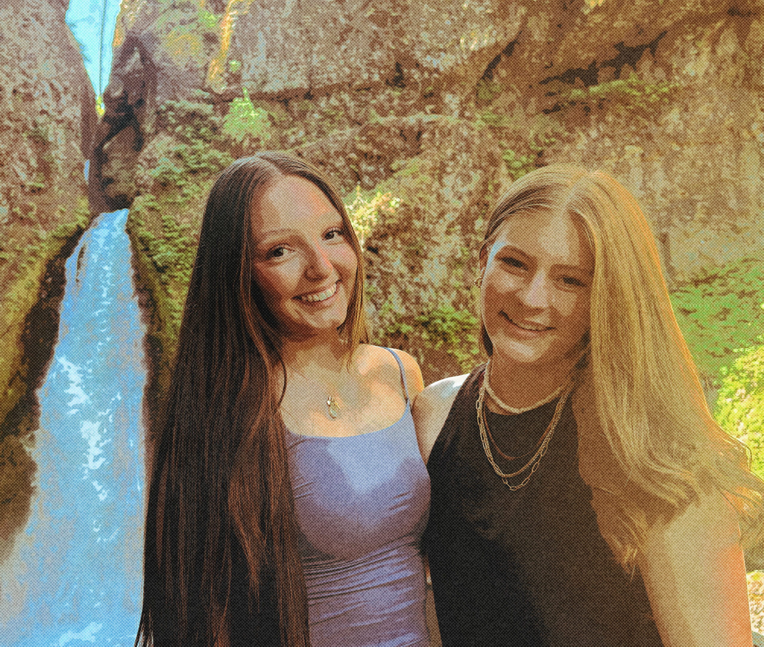 Two teenage girls standing in front of waterfall
